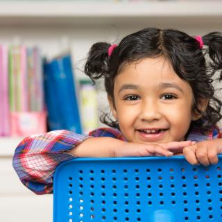 little girl looking over the back of a chair smiling at the camera