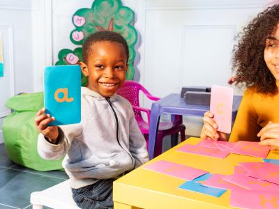 child holding up card with the letter A