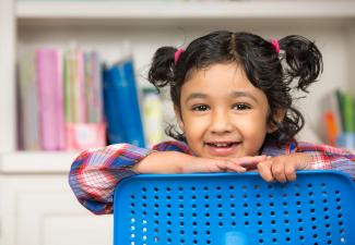 little girl looking over the back of a chair smiling at the camera